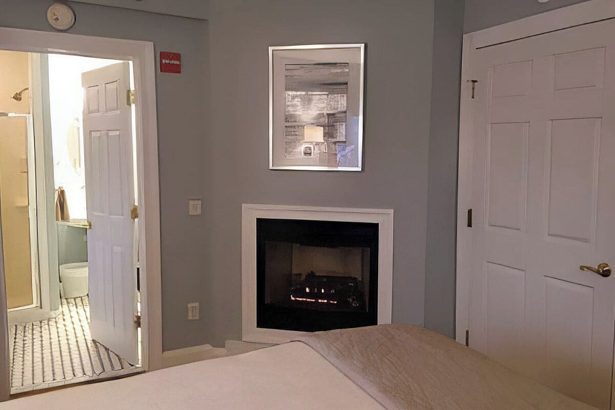 A hotel room with a bed, a fireplace, and a door leading to a bathroom.