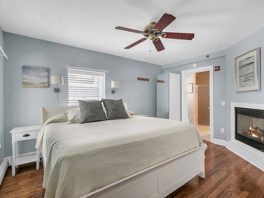 A bedroom with a bed, a ceiling fan, a fireplace, and a nightstand.