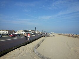Un paseo marítimo con un muelle de madera, playa de arena y edificios al fondo.