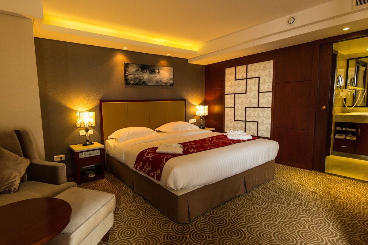 A hotel room with a bed, a chair, a nightstand, and a small table.