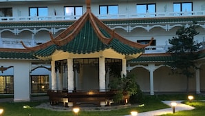 A traditional pavilion with a tiled roof, surrounded by a stone pathway and illuminated by ground lights. - Huatian Chinagora Hotel (Alfortville)