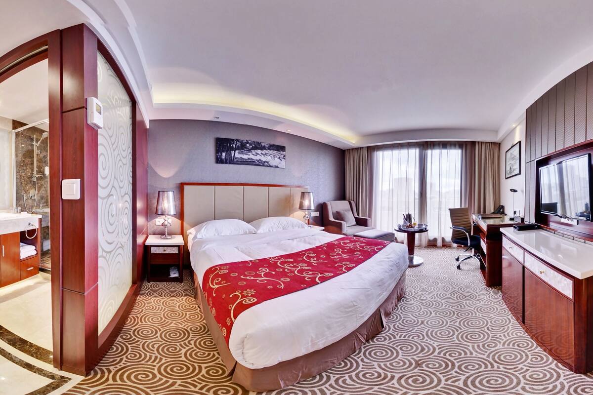 A hotel room with a bed, a desk, a vanity, and a shower area.