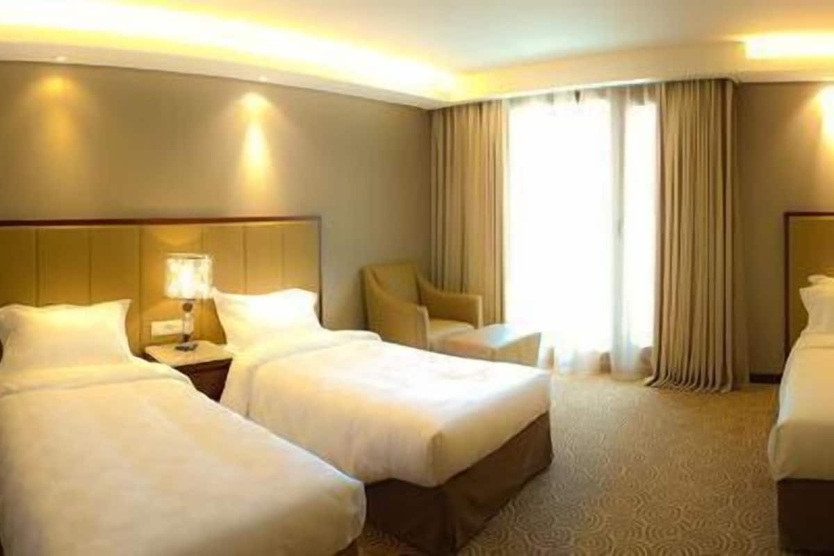 A hotel room with two beds, a desk, a chair, a TV, and a window with curtains.