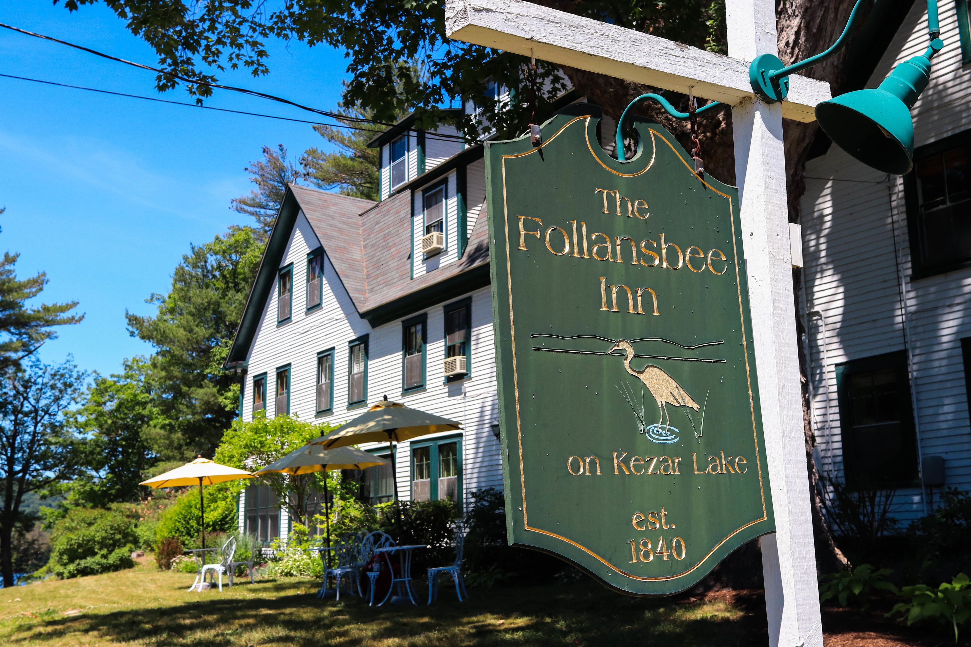 A green sign for The Follanshee Inn on Kear Lake, established in 1840, with outdoor seating and umbrellas.