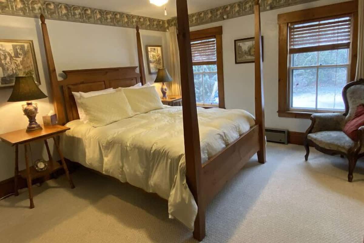 A four-poster bed with white linens, a wooden headboard, and a nightstand with a lamp.