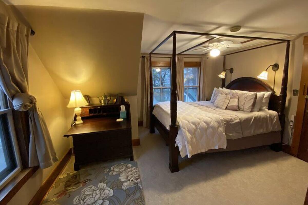 A four-poster bed with a wooden frame, a bedside table with a lamp, and a floral-patterned rug.