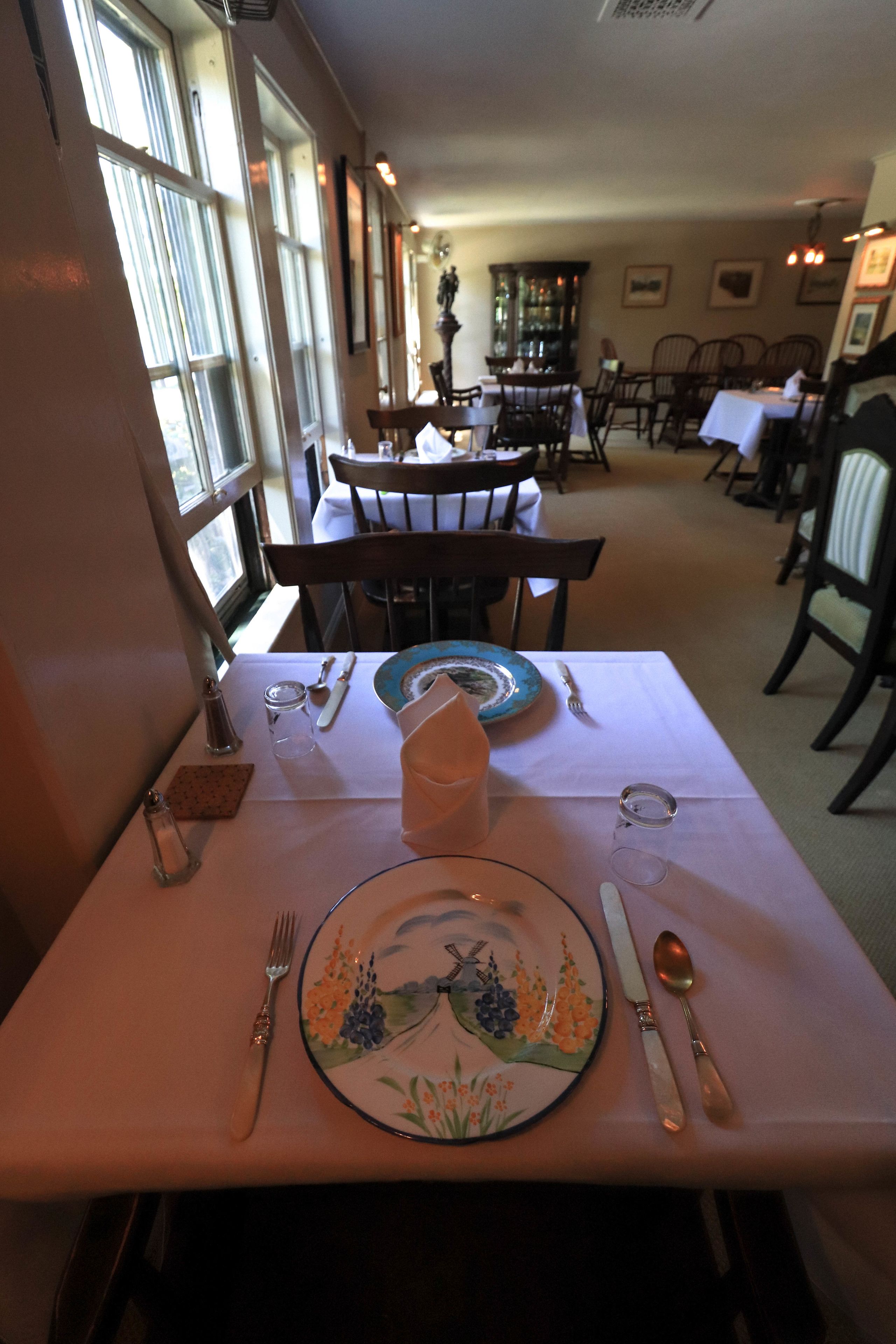 A dining area with tables set for two, featuring a decorative plate and cutlery.