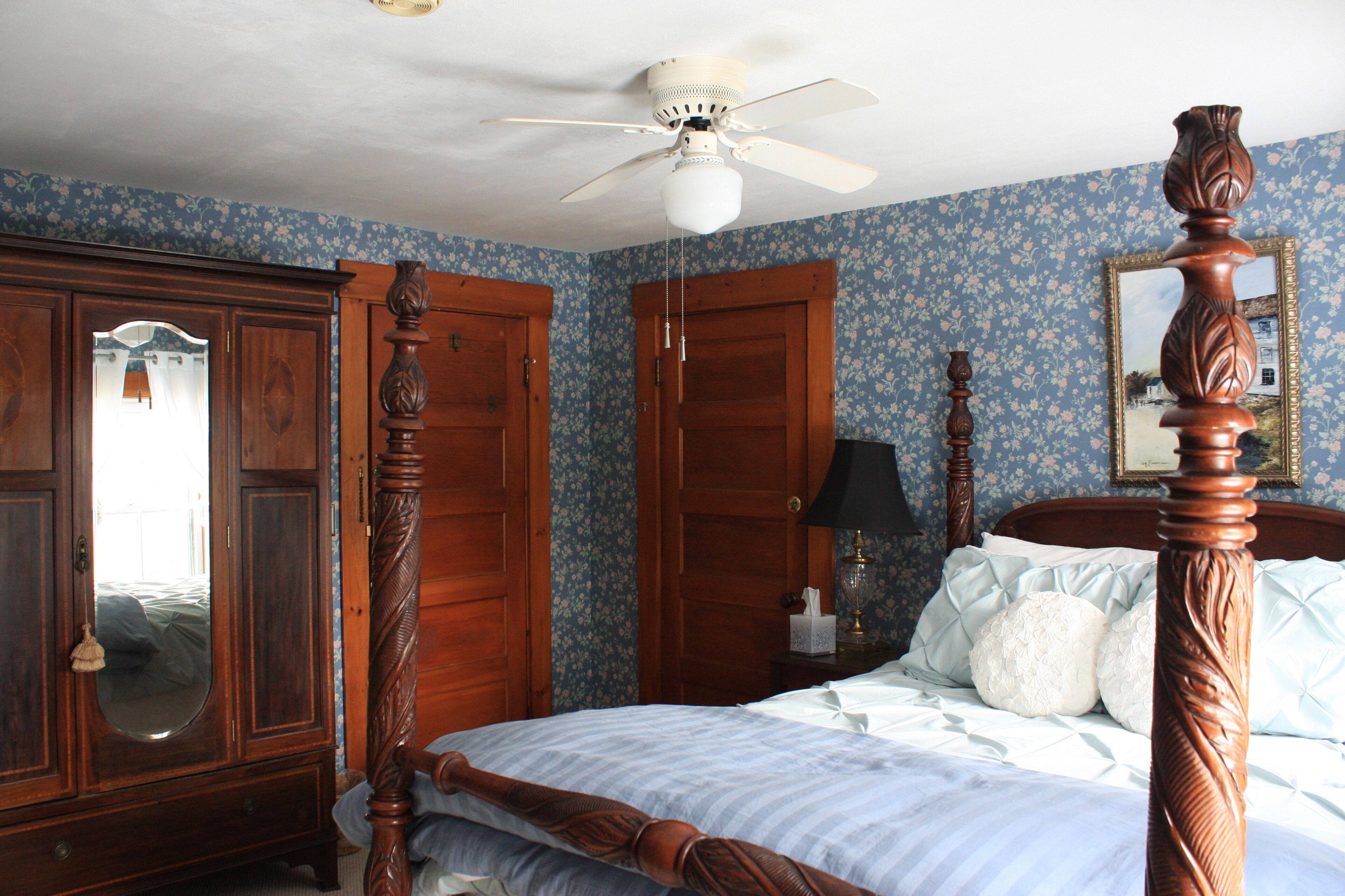 Une chambre à coucher avec un lit à baldaquin, une armoire en bois et un ventilateur de plafond.