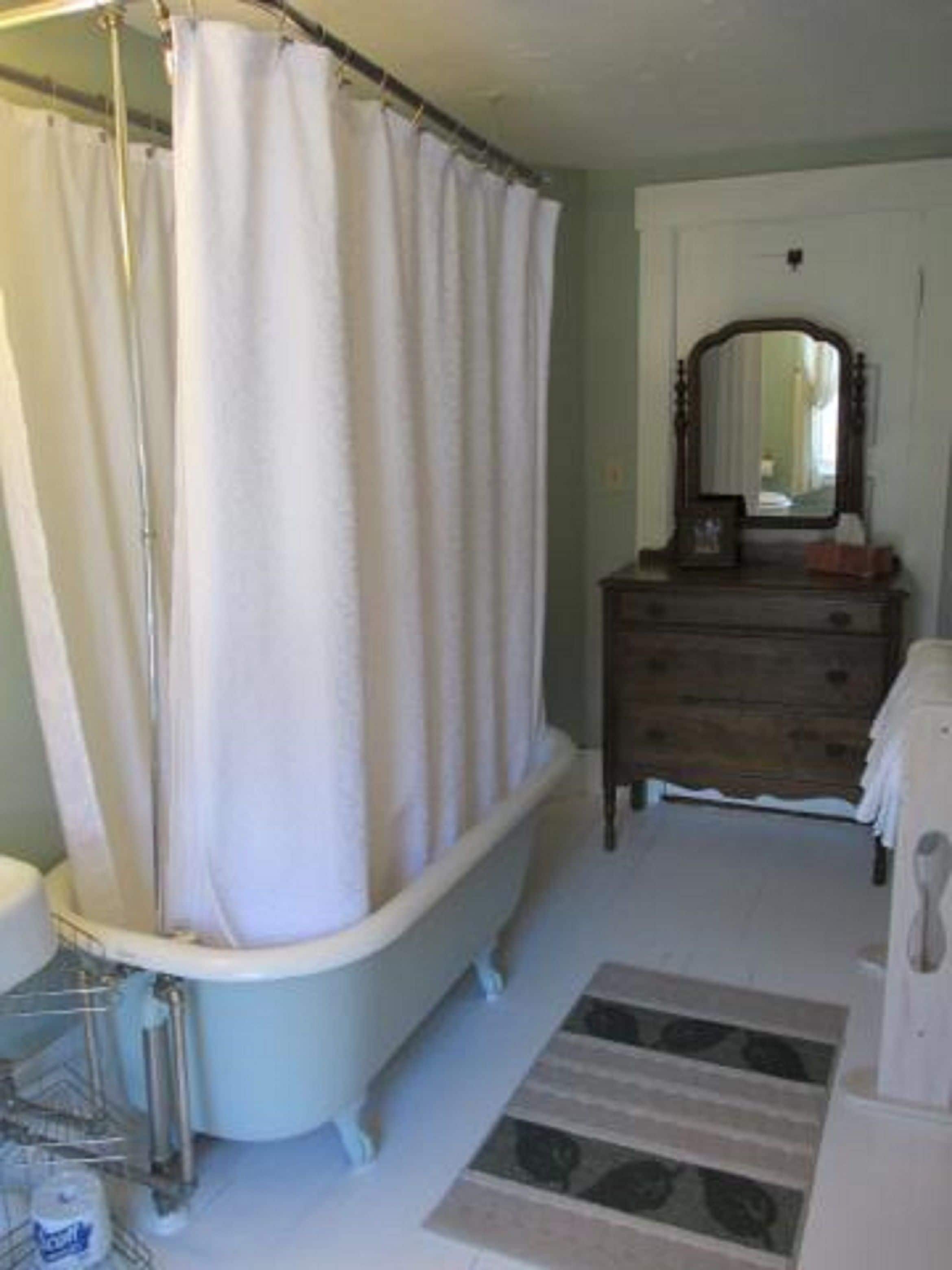 A bathroom with a clawfoot bathtub, a wooden dresser, and a mirror.