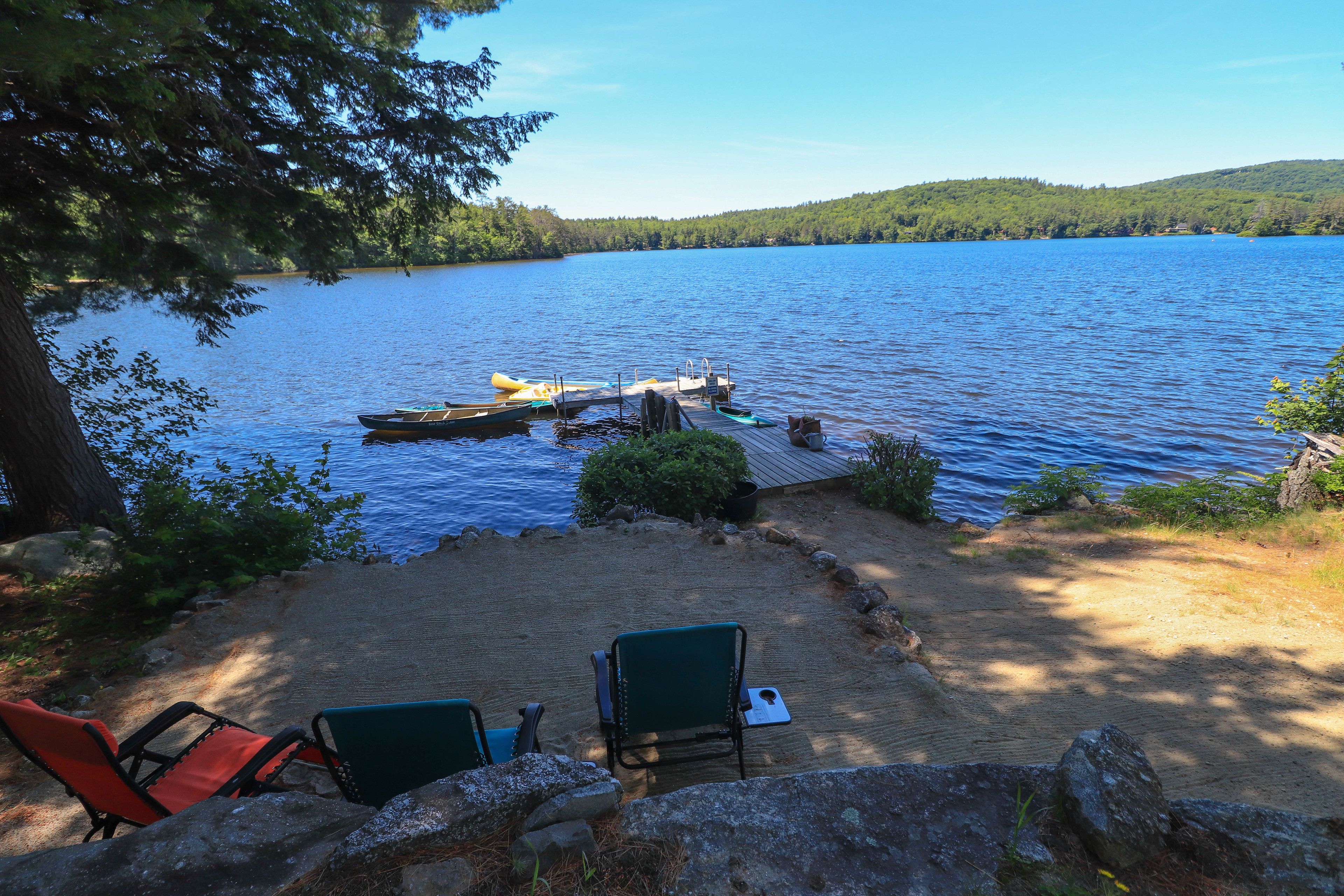 A lakeside deck with two green chairs, a dock with a kayak, and a clear view of the lake.