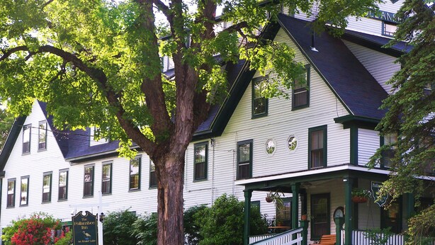 A traditional two-story house with a porch and a large tree in front.