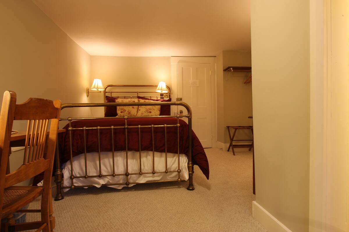 A bedroom with a metal bed frame, a wooden chair, a bedside table, and a lamp.