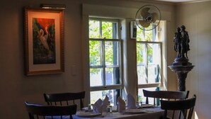 A dining area with a table set for four, a painting on the wall, and a statue on a pedestal.