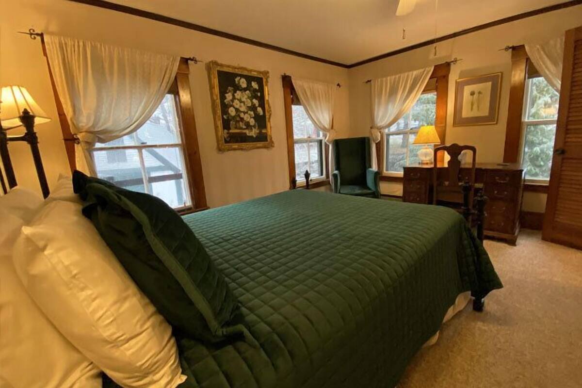 A bedroom with a large bed, a chair, a dresser, and a window with curtains.