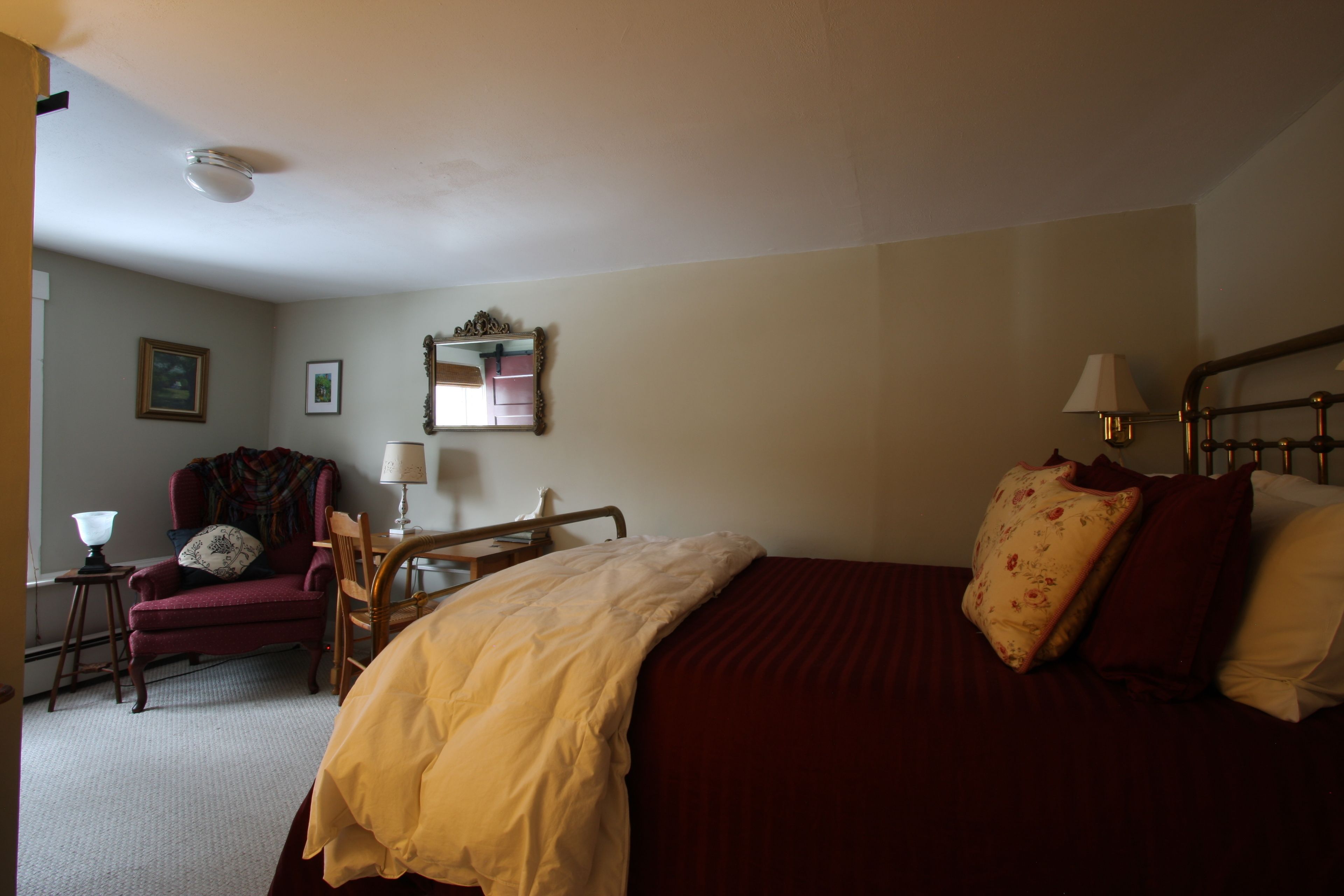 A hotel room with a bed, a chair, a desk, a lamp, and a mirror.