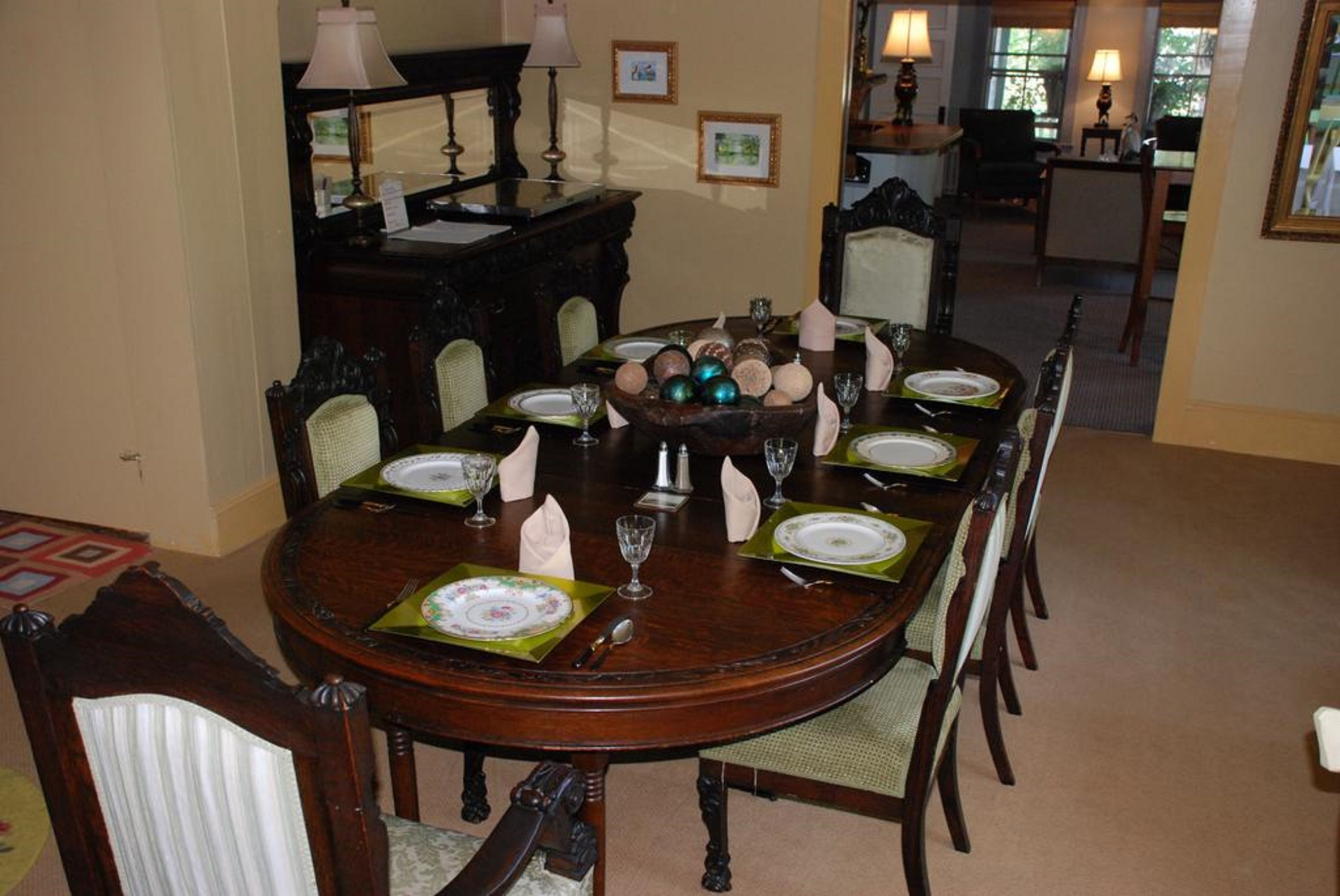 A dining room with a round table set for six, surrounded by upholstered chairs.