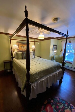 A four-poster bed with a canopy, a nightstand, a lamp, and a window with curtains.