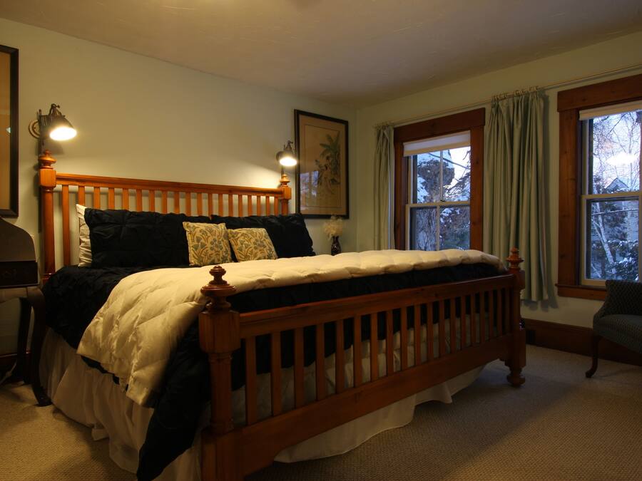Een slaapkamer met een houten bed, twee bedlampen, een stoel en een raam met gordijnen.