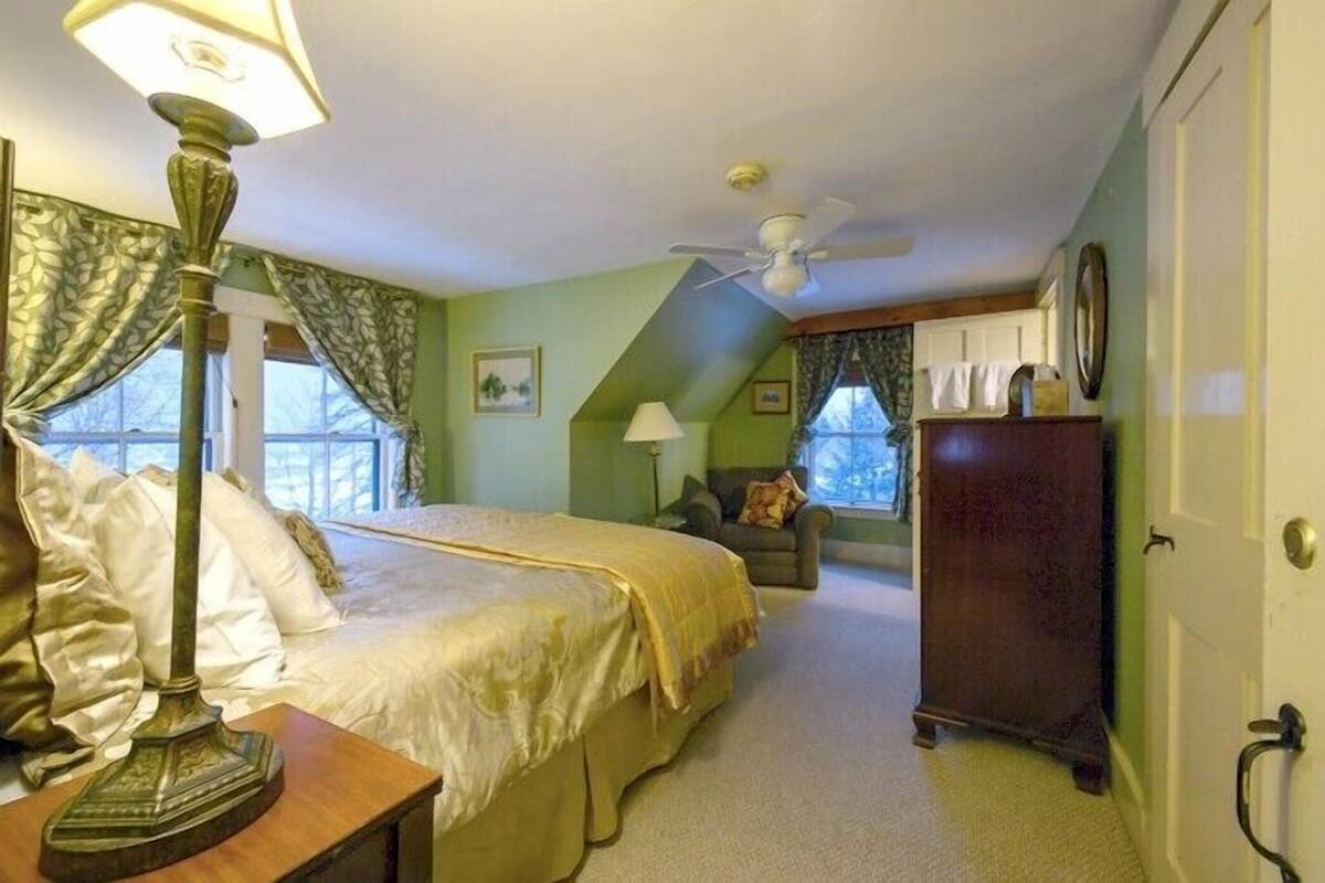 A bedroom with a bed, a nightstand, a lamp, a dresser, a chair, and a ceiling fan.