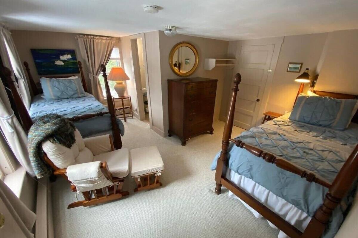 A bedroom with two double beds, a wooden rocking chair, a dresser, and a mirror.