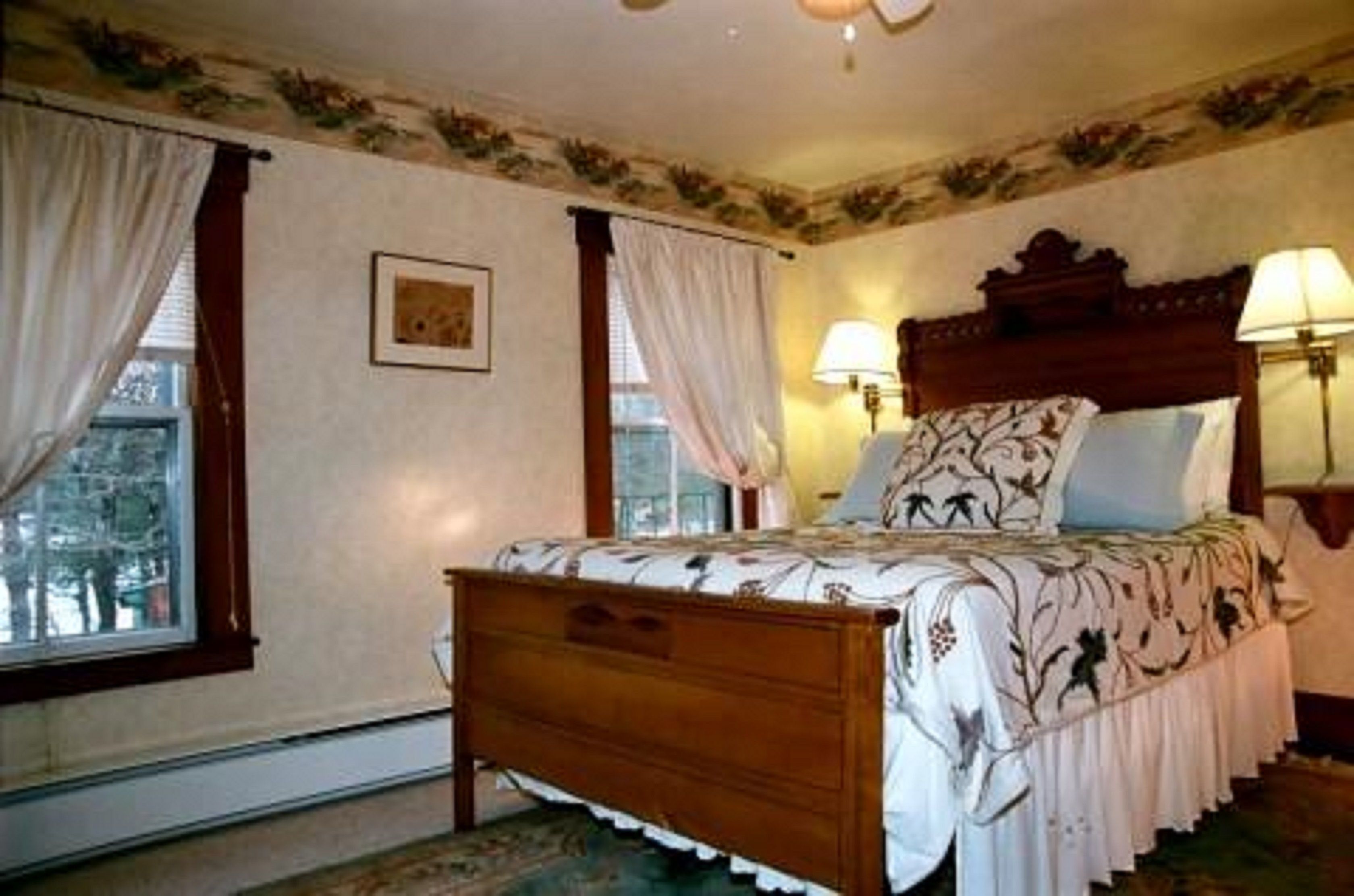 A bedroom with a wooden bed, two bedside lamps, and a window with curtains.