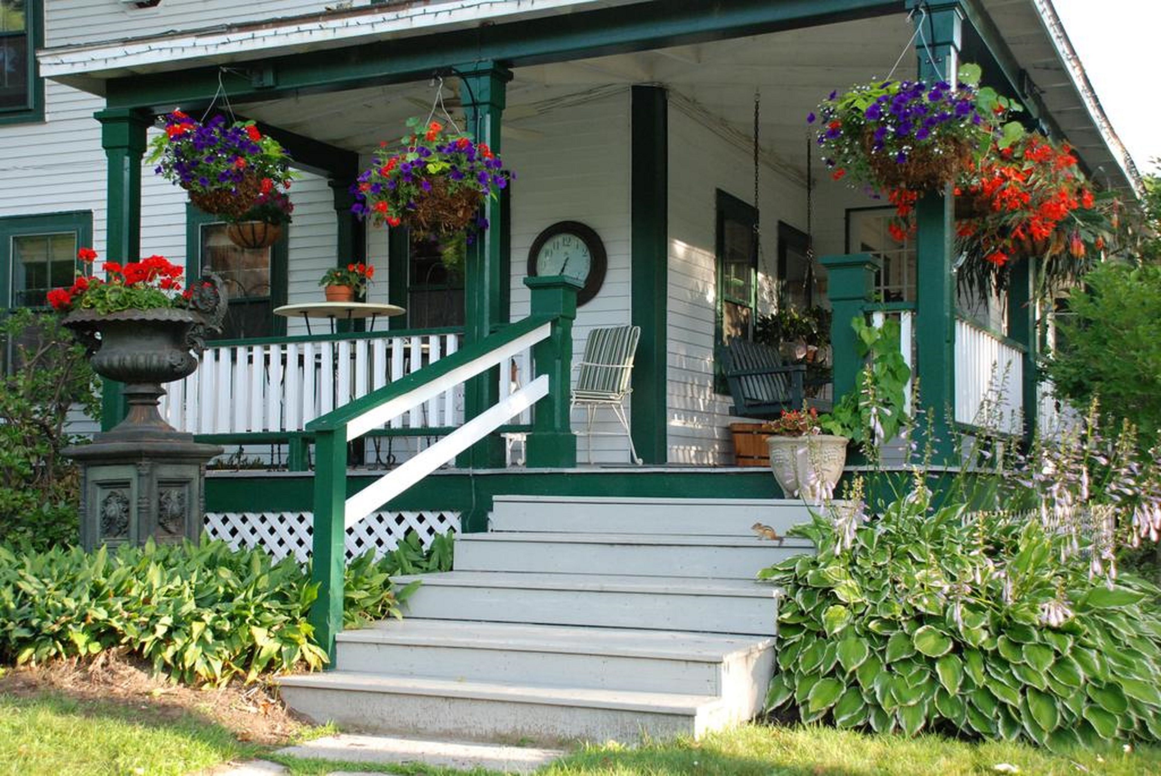 A porch with steps, a white fence, and hanging flower baskets.