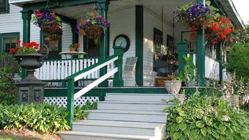 A porch with steps, a white fence, and hanging flower baskets.