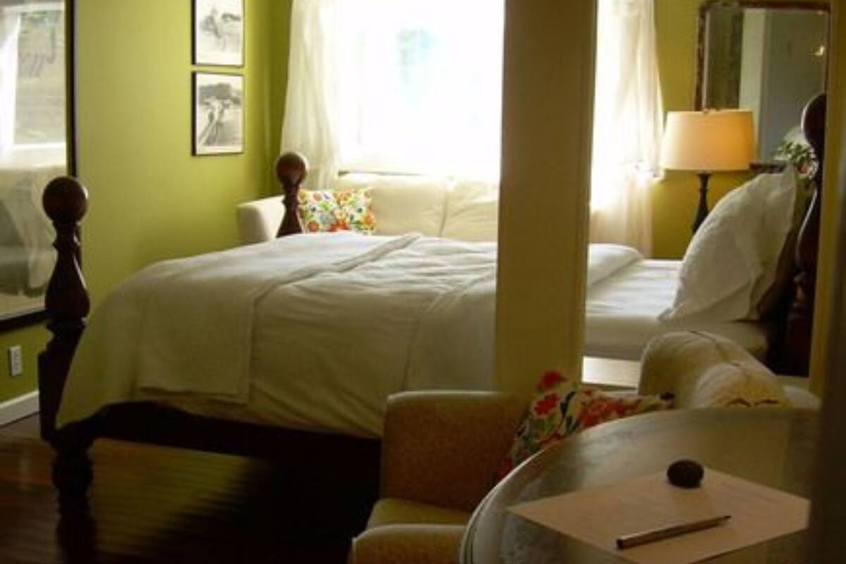 A hotel room with a bed, a chair, a table, and a lamp.