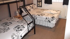 Quarto em dormitório com beliches, uma cama grande com roupa de cama floral, um espelho e um radiador.