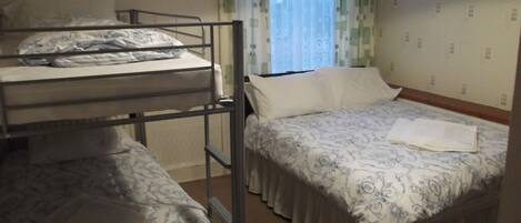 A dormitory room with bunk beds, a bedside table with a lamp, and a window with curtains.