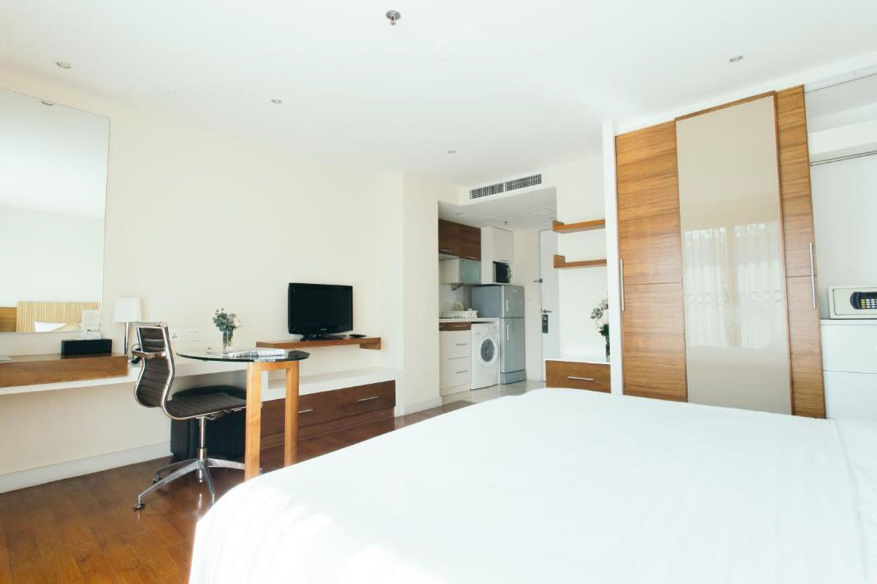 Quarto de hotel com cama, secretária com cadeira, televisão, guarda-roupa e cozinha compacta.
