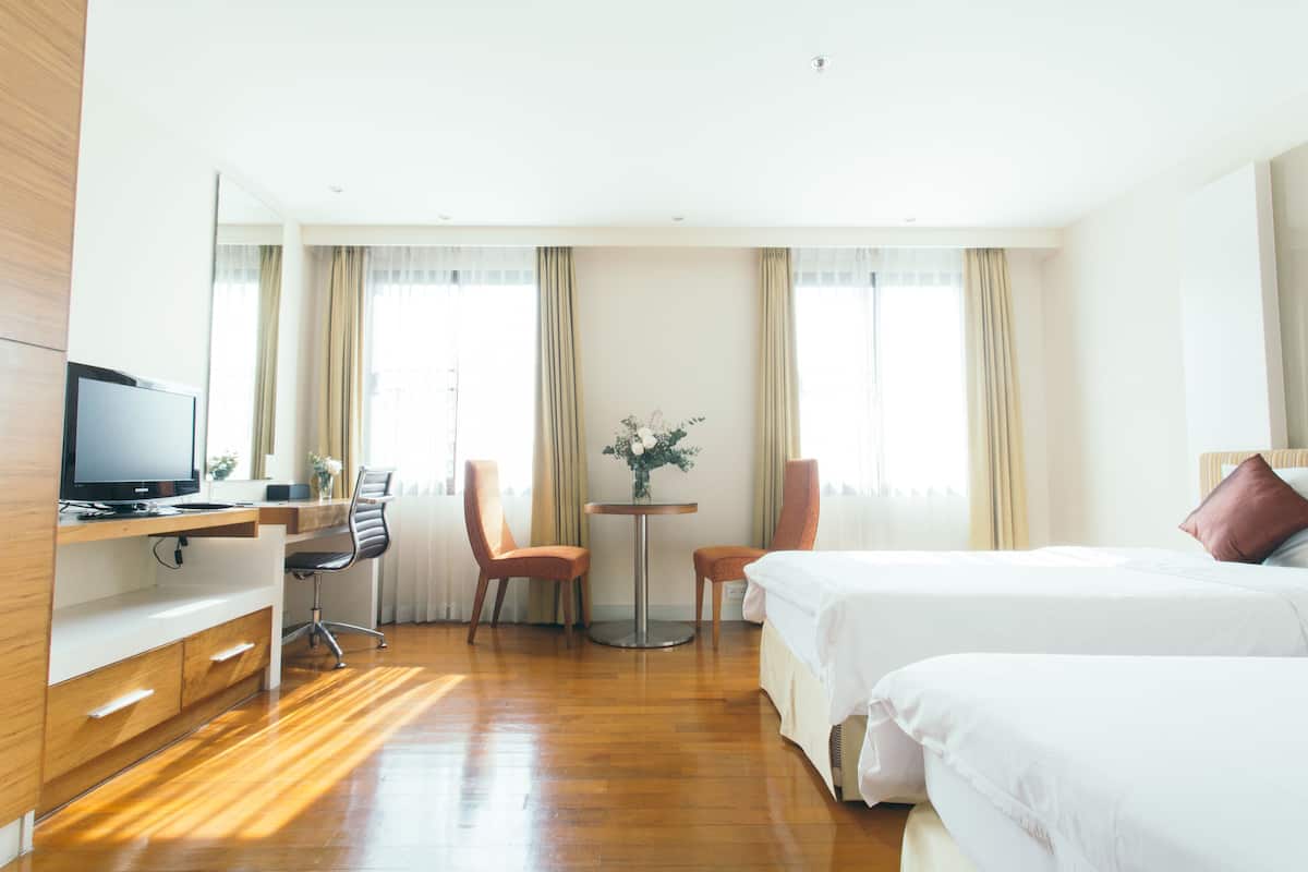 Ein Hotelzimmer mit einem Holztisch, einem Fernseher, zwei Stühlen, einem runden Tisch mit einer Vase und zwei Betten.