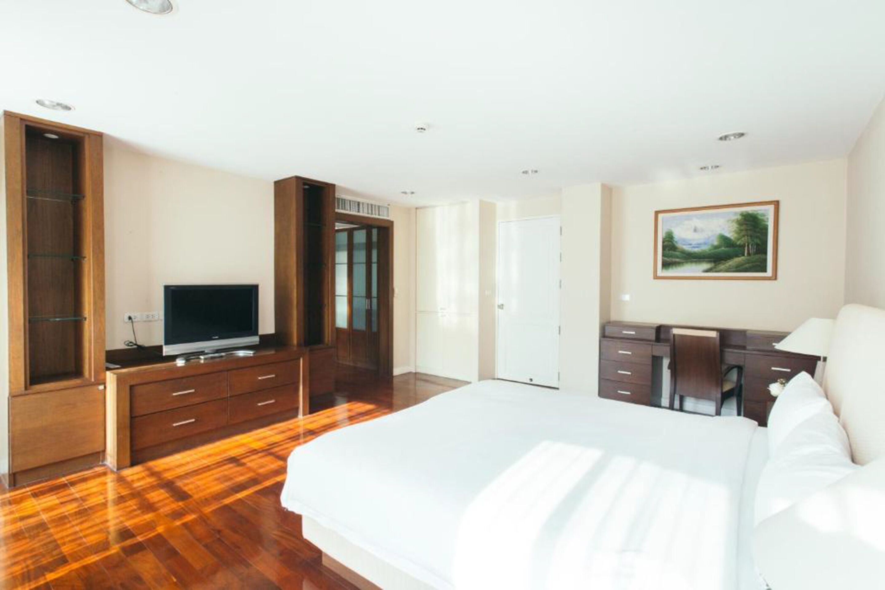 A modern hotel room with a large bed, wooden flooring, a flat-screen TV, a desk with a chair, and a painting on the wall.
