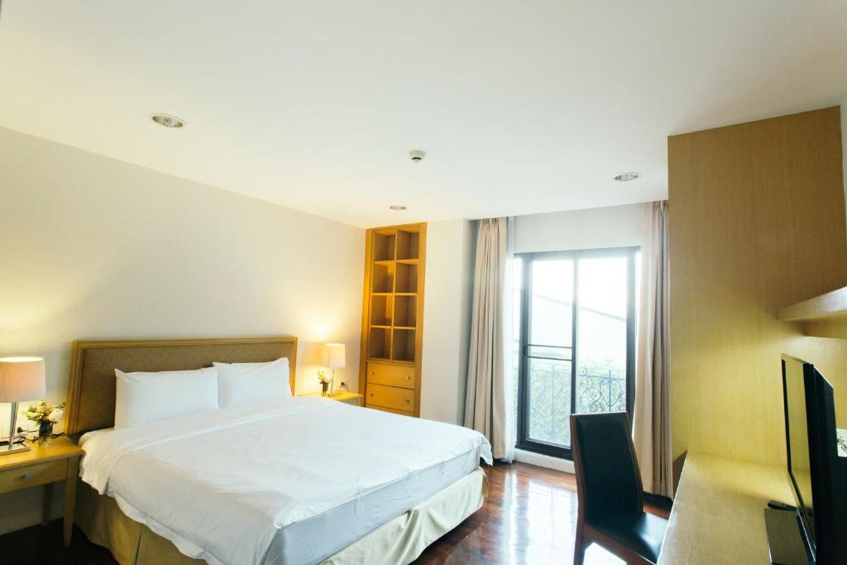 A hotel room with a large bed, a desk with a chair, a TV, and a window with curtains.