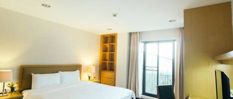 A hotel room with a large bed, a desk with a chair, a TV, and a window with curtains.