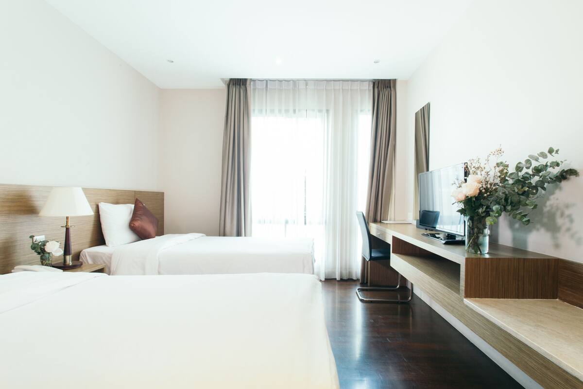 Ein Hotelzimmer mit zwei Betten, einem Schreibtisch, einem Fernseher und einem Fenster mit Vorhängen.