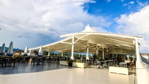 An outdoor seating area with umbrellas and tables, a covered pavilion, and a view of the sea and mountains in the background. - Boracay Uptown (Boracay Island)