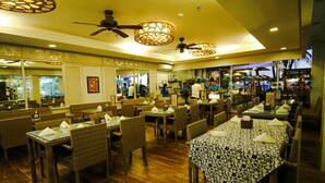 A restaurant with wicker chairs and tables, ceiling fans, and a view of the street. - Boracay Uptown (Boracay Island)