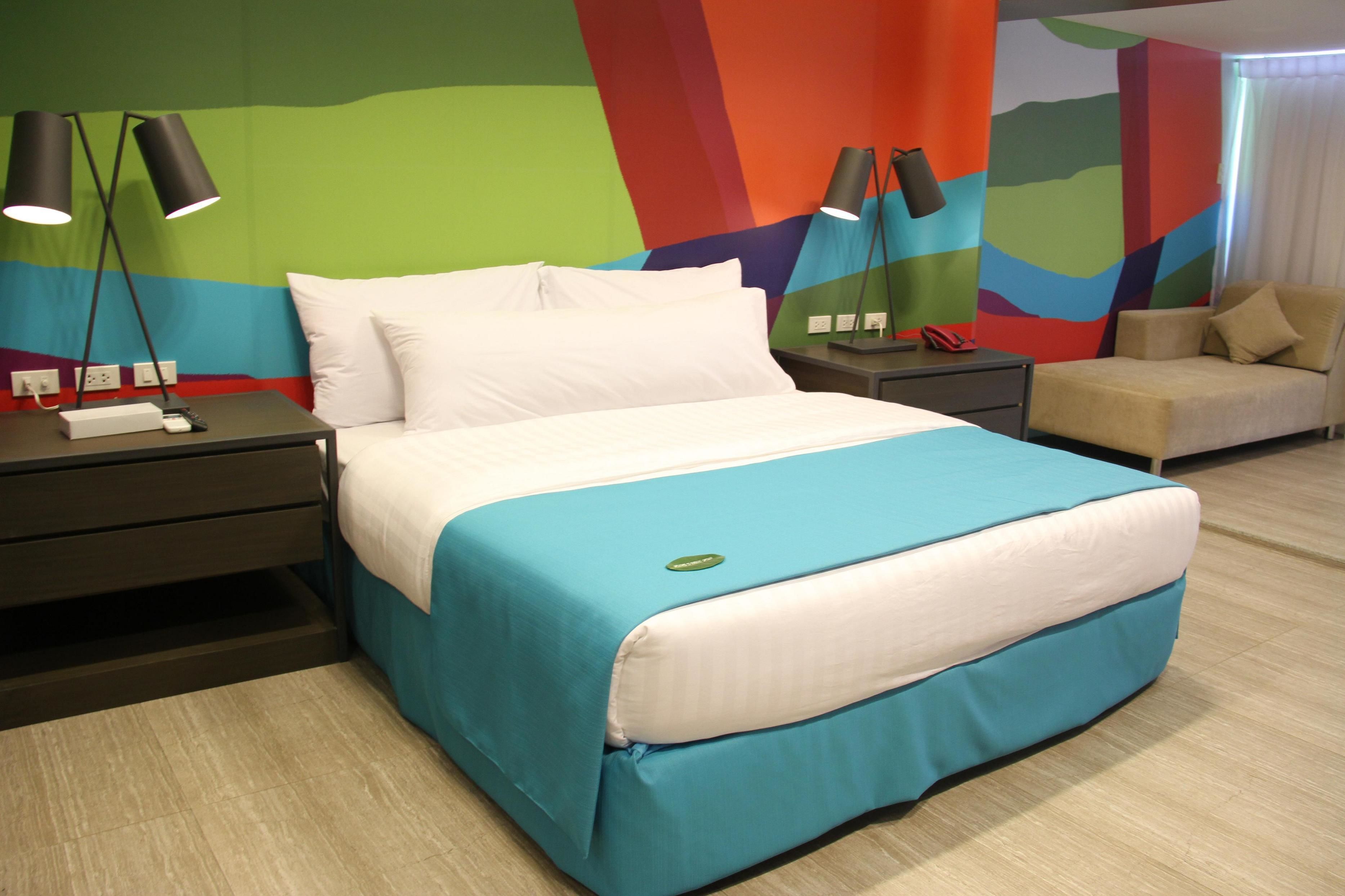 Habitación de hotel con una cama, mesitas de noche, una lámpara y una silla.