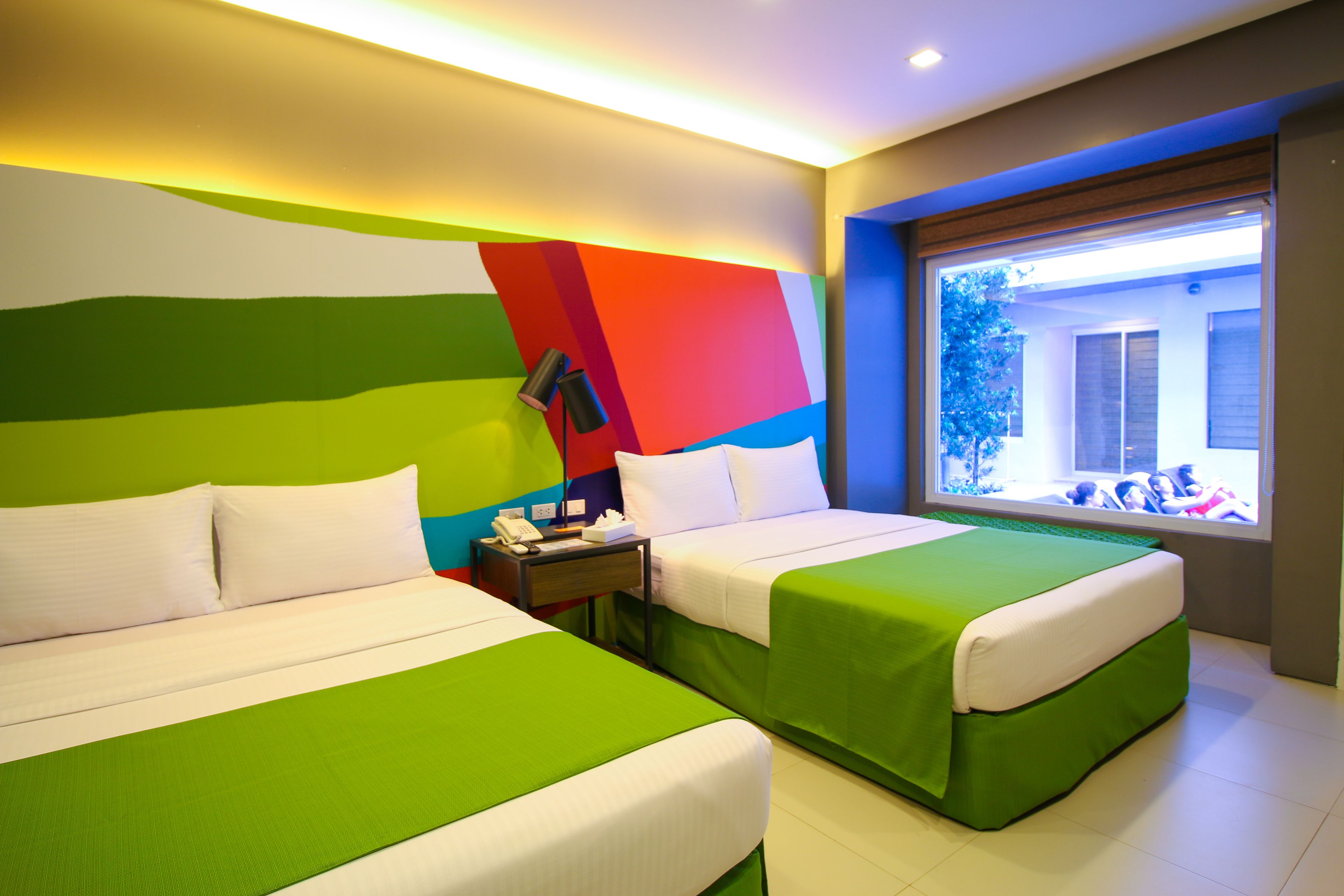 A hotel room with two beds, a nightstand, and a window with a view of the outside.