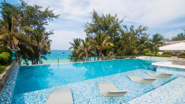 A clear blue pool with lounge chairs, surrounded by palm trees and a view of the ocean. - Boracay Uptown (Boracay Island)