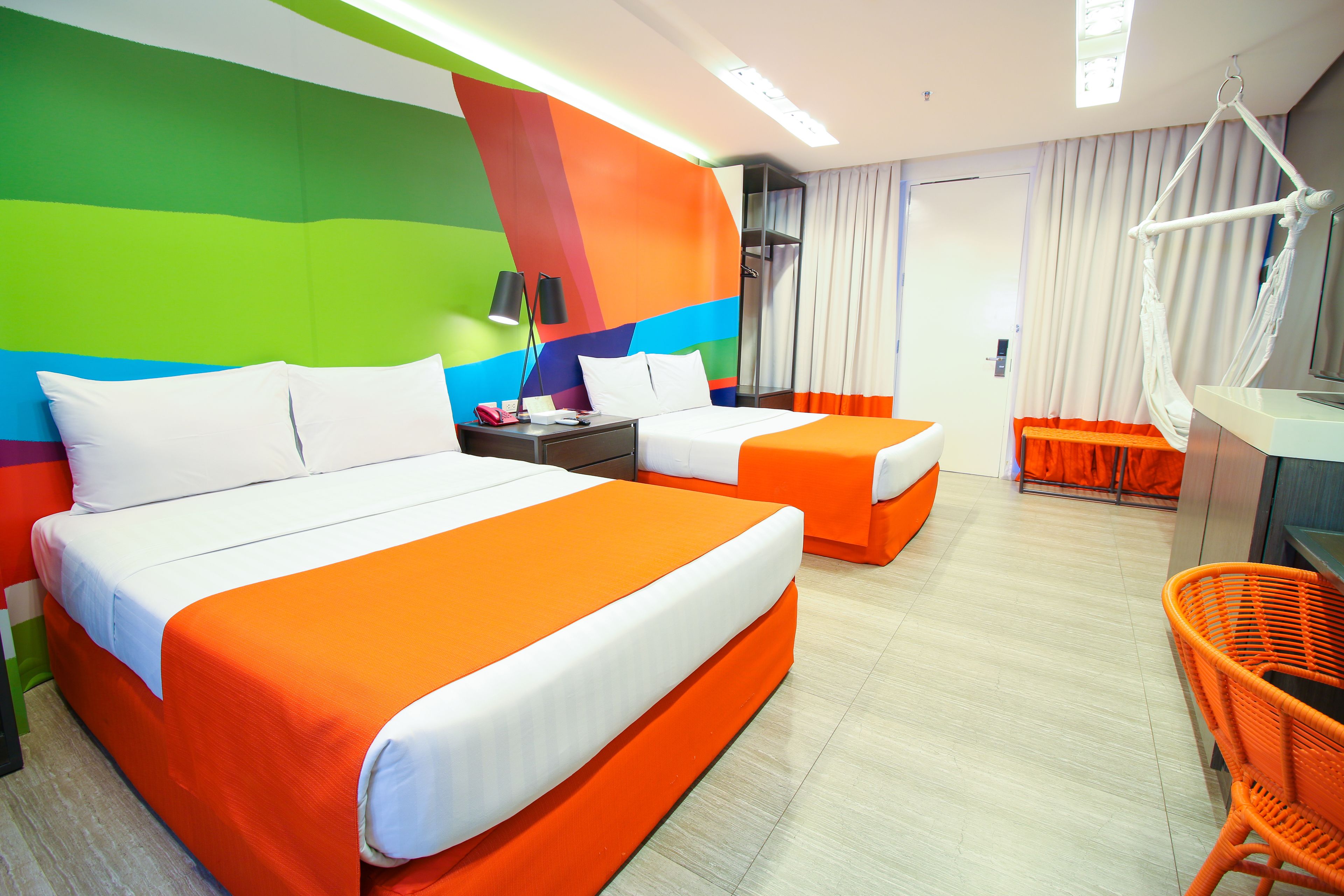 Habitación de hotel con dos camas, una silla colgante y un ventanal con cortinas.