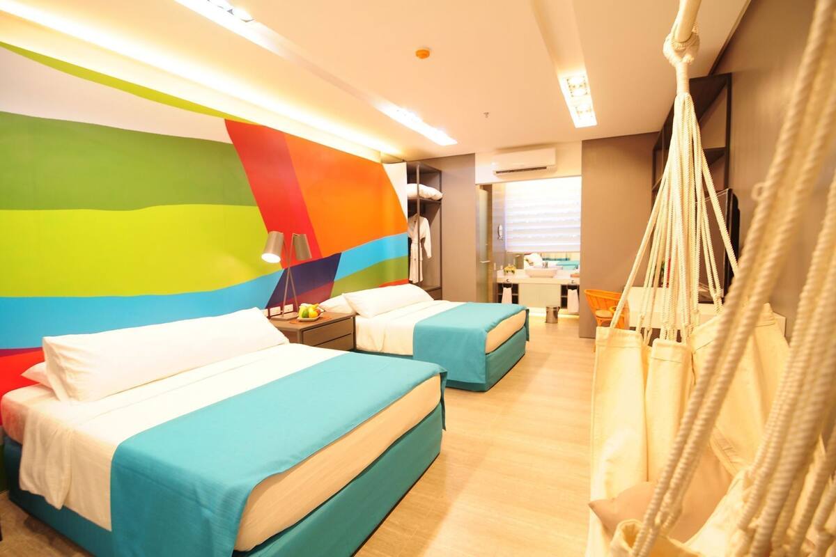 Habitación de hotel con dos camas, una pared de colores vivos, un sillón colgante y vistas a la cocina.