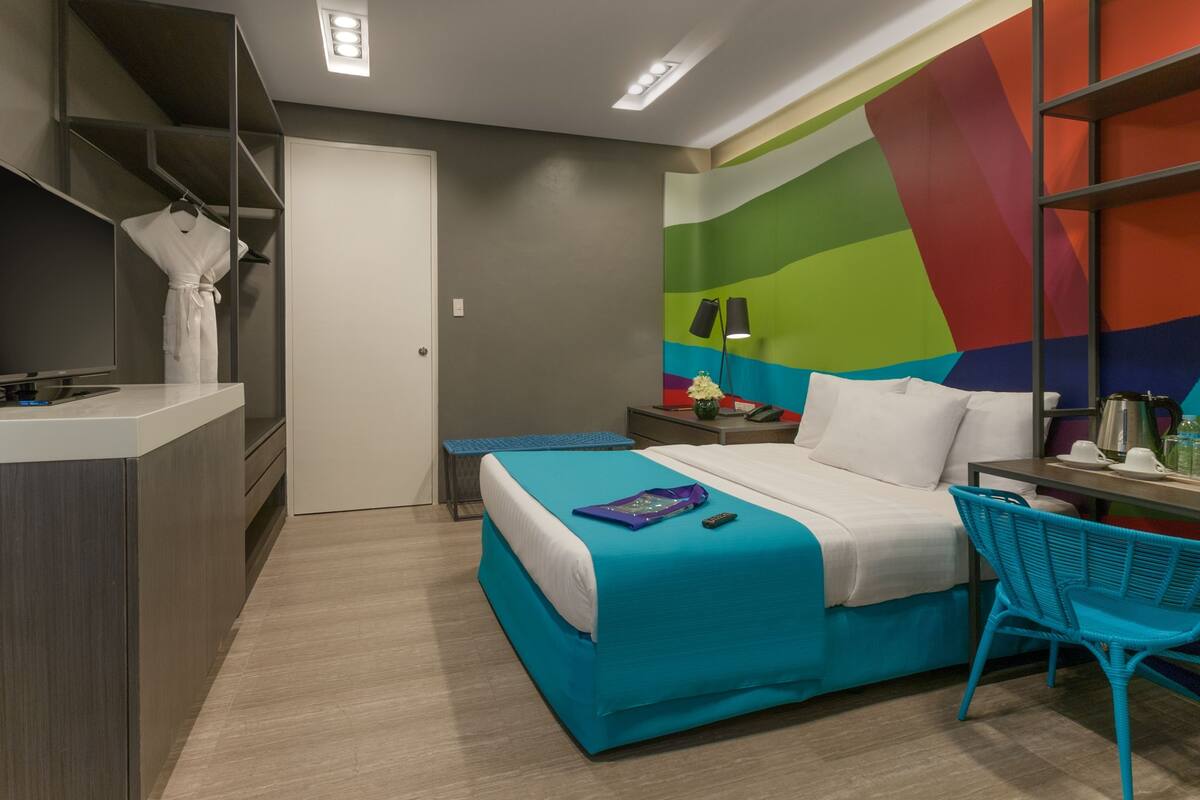 Una habitación de hotel moderna con una cama, un escritorio, una silla y una pared colorida.