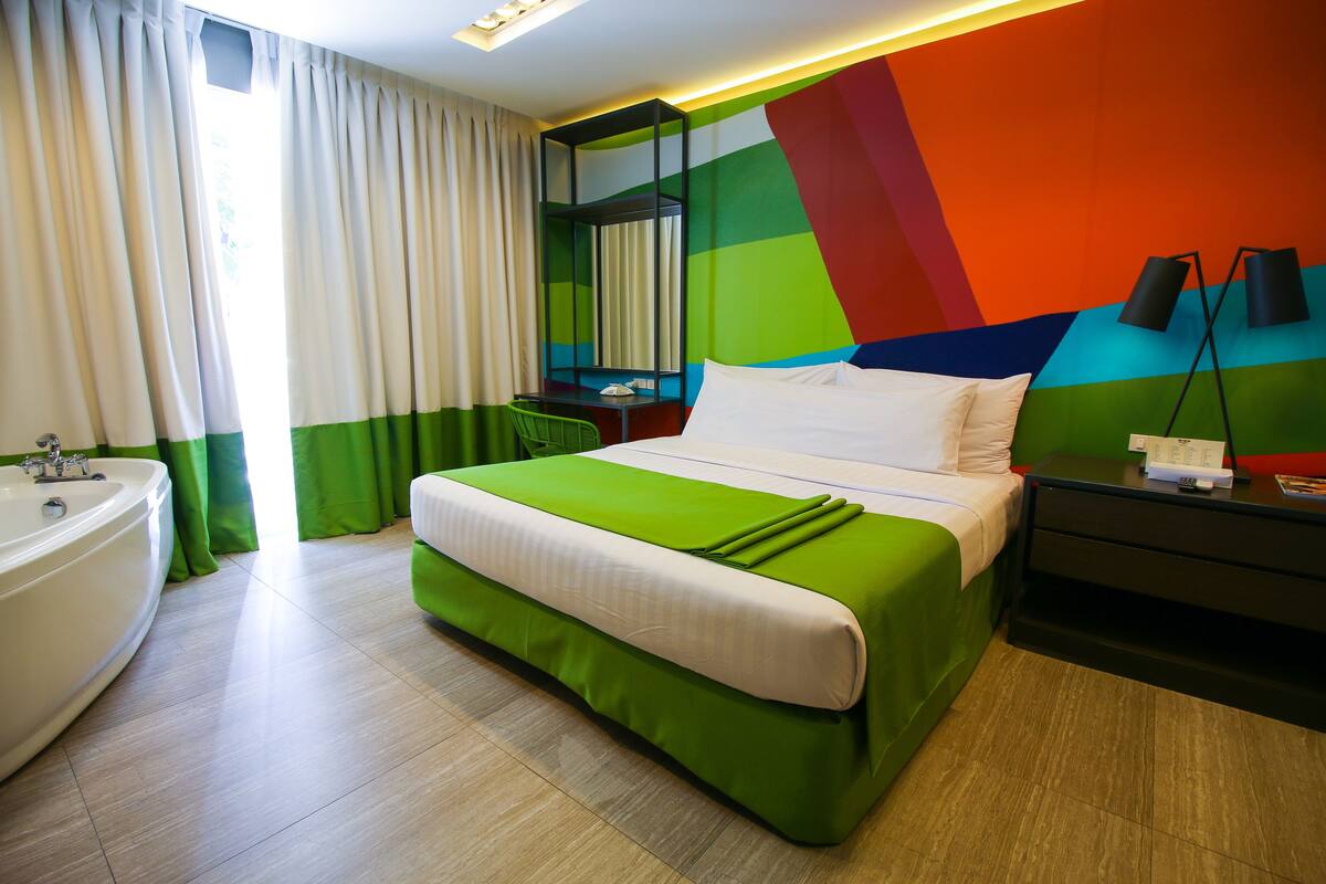 Una habitación de hotel moderna con una cama grande, una decoración en tonos verde y blanco, un baño con bañera y un diseño de pared colorido.