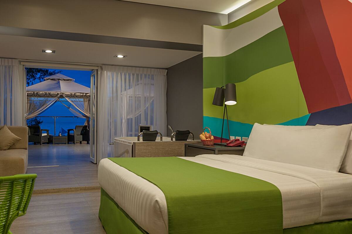 Habitación de hotel con cama, escritorio, silla, lámpara y vista al exterior.
