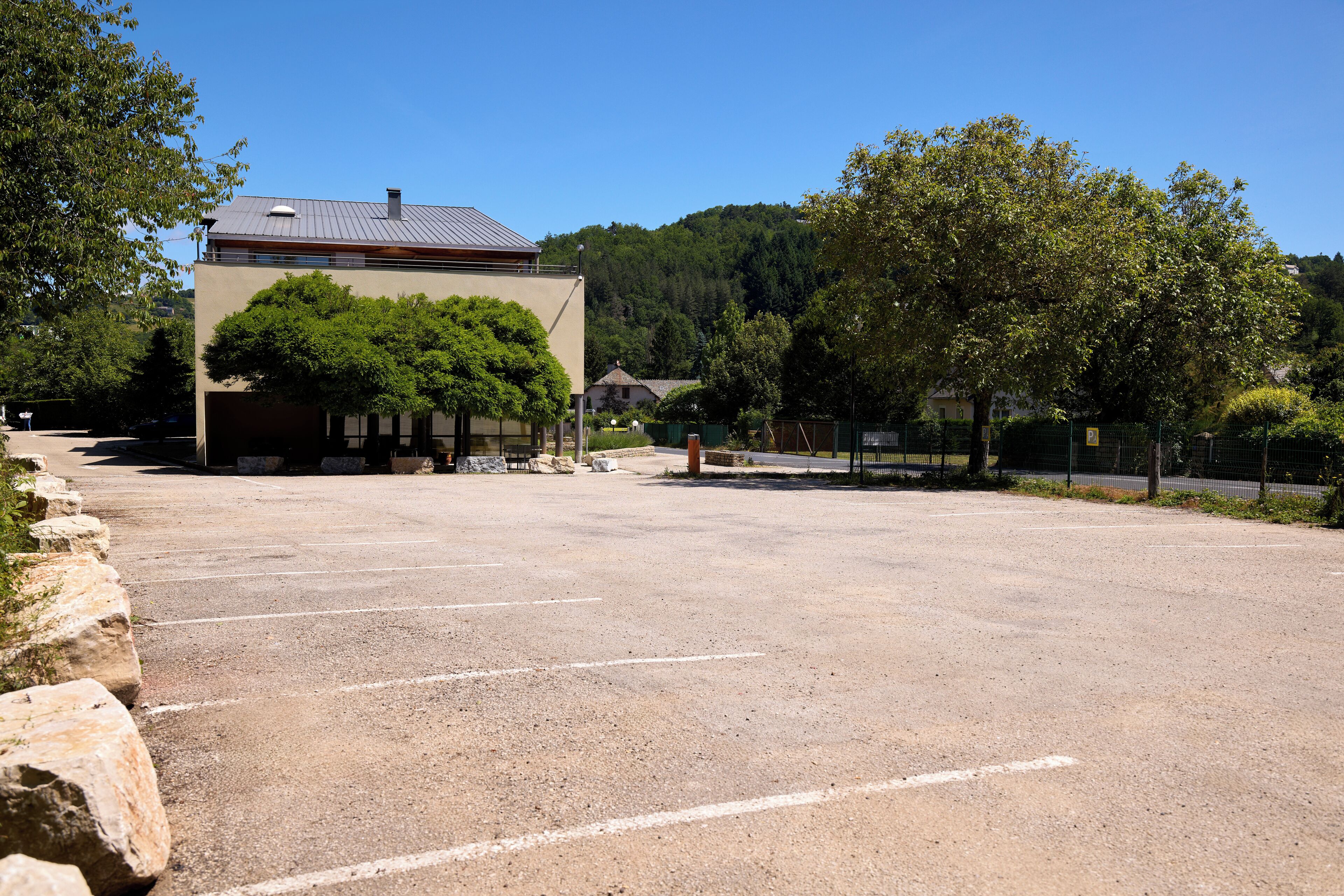 Un estacionamiento con un edificio al fondo, rodeado de árboles y un paisaje montañoso.