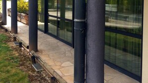 A building with a covered patio area, large glass windows, and black columns. - Hôtel Eco (Banassac)