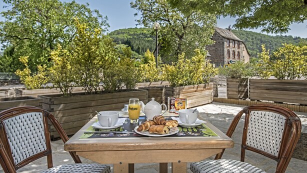 An outdoor dining area with a table set for two, featuring a plate of croissants, a teapot, cups, and a glass of orange juice. - Hôtel Eco (Banassac)