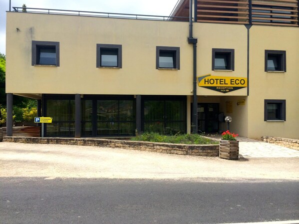 A hotel named HOTEL ECO with a reception area, large windows, and a stone planter with flowers. - Hôtel Eco (Banassac)
